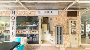 A hotel entrance with a sign reading "HOTEL SANTA TERESITA," a glass door, a staircase leading inside, and a small outdoor seating area with a table and chairs.