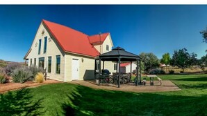 A house with a red roof, a covered patio with outdoor furniture, and a well-maintained lawn. - Homestead Hideaway- Spacious Home Central to Zion, Grand Canyon, Bryce & More! (Cane Beds)