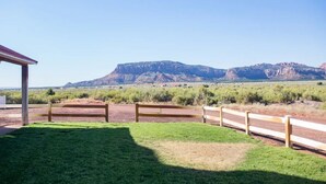 A grassy area with a wooden fence and a building in the foreground, with a mountain range in the background. - Homestead Hideaway- Spacious Home Central to Zion, Grand Canyon, Bryce & More! (Cane Beds)