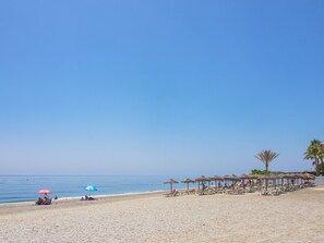 A beach with sun loungers and umbrellas, a clear sky, and a calm sea.