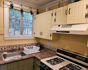 A kitchen with a gas stove, a sink, and a window with a view of trees.