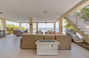 A spacious outdoor living area with a wicker sofa, a dining table, and a hammock. A staircase leads to an upper level.