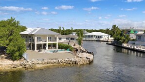 Ein Anwesen am Wasser mit einem großen Haus, das einen Balkon, einen Pool und eine Steinmauer hat.