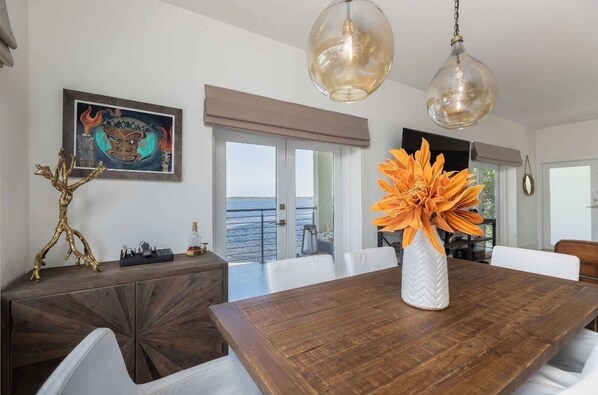 A dining area with a wooden table, white chairs, a decorative vase with orange flowers, and a painting on the wall.