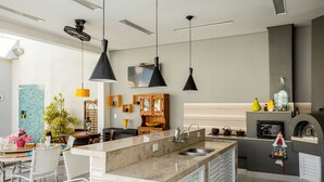 A modern kitchen with a central island, pendant lighting, and a built-in oven. - Casa Indaiá - Caraguatatuba (Caraguatatuba)