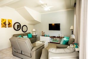 Uma sala de estar moderna com sofá, poltronas, mesa de centro e televisão de tela plana na parede.