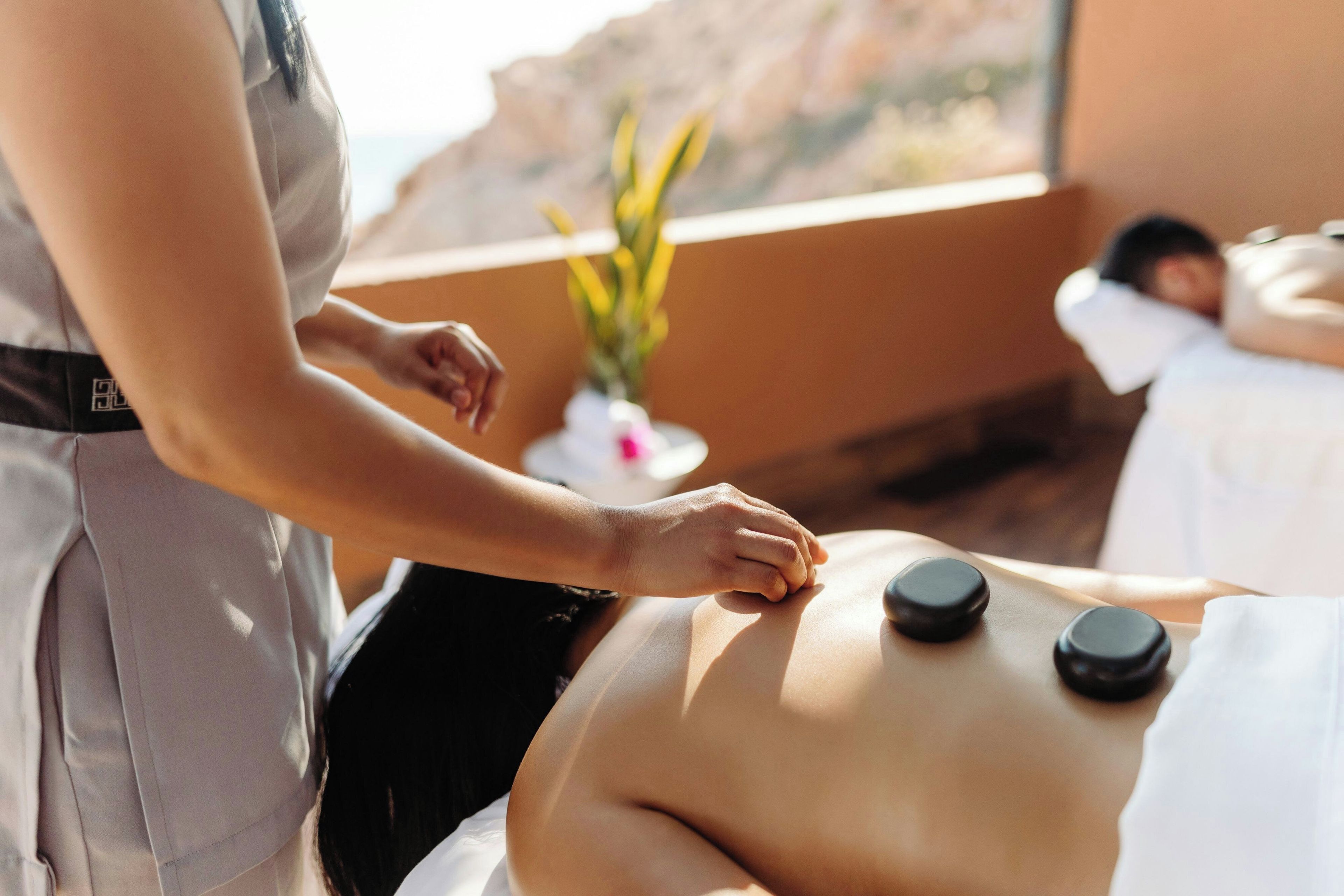 En massageterapeut giver en massage, hvor klienten ligger på maven, mens terapeuten arbejder med et værktøj.