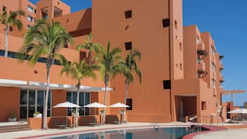 A hotel with a swimming pool, palm trees, and a modern architectural design.