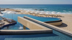 A pool area with a water slide, lounge chairs, and umbrellas, overlooking a beach and the ocean. - The Westin Los Cabos Resort Villas - Baja Point (San José del Cabo)