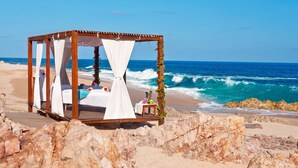 Un quiosco en la playa con una cama, una mesita y una silla.