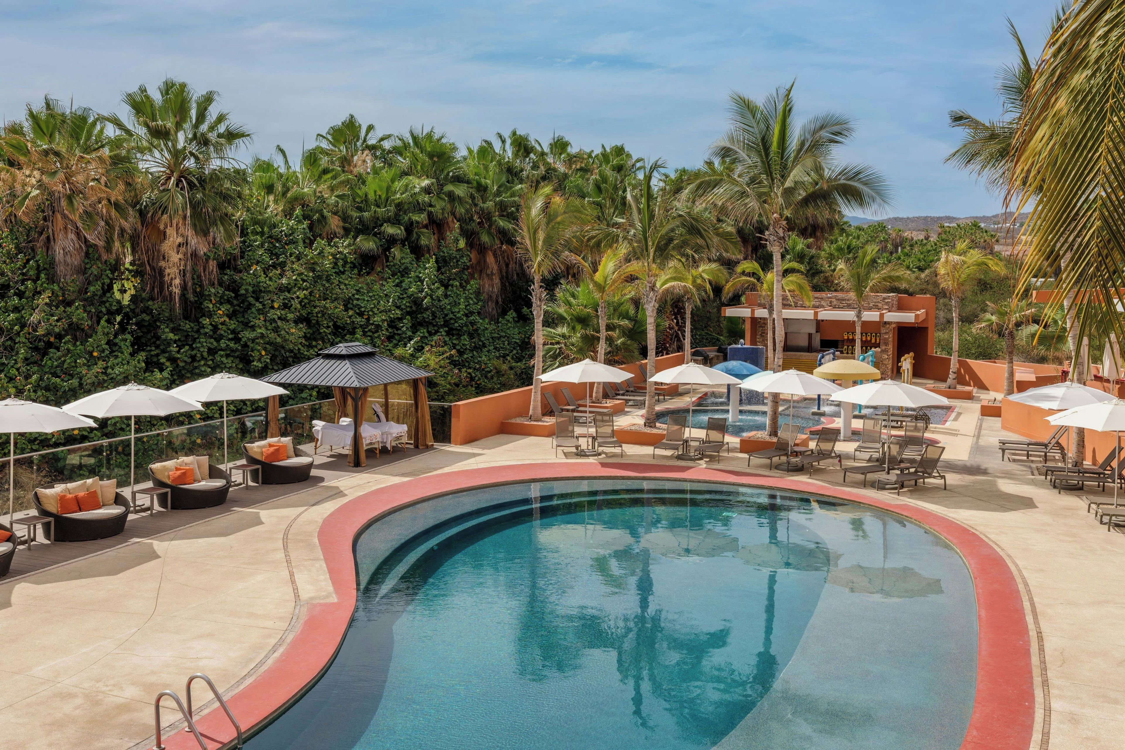 Área de piscina en un resort con sillones, sombrillas y vista despejada de la vegetación tropical circundante.
