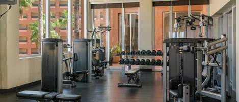 Ett gym med olika typer av träningsutrustning, inklusive styrketräningsmaskiner och hantlar.