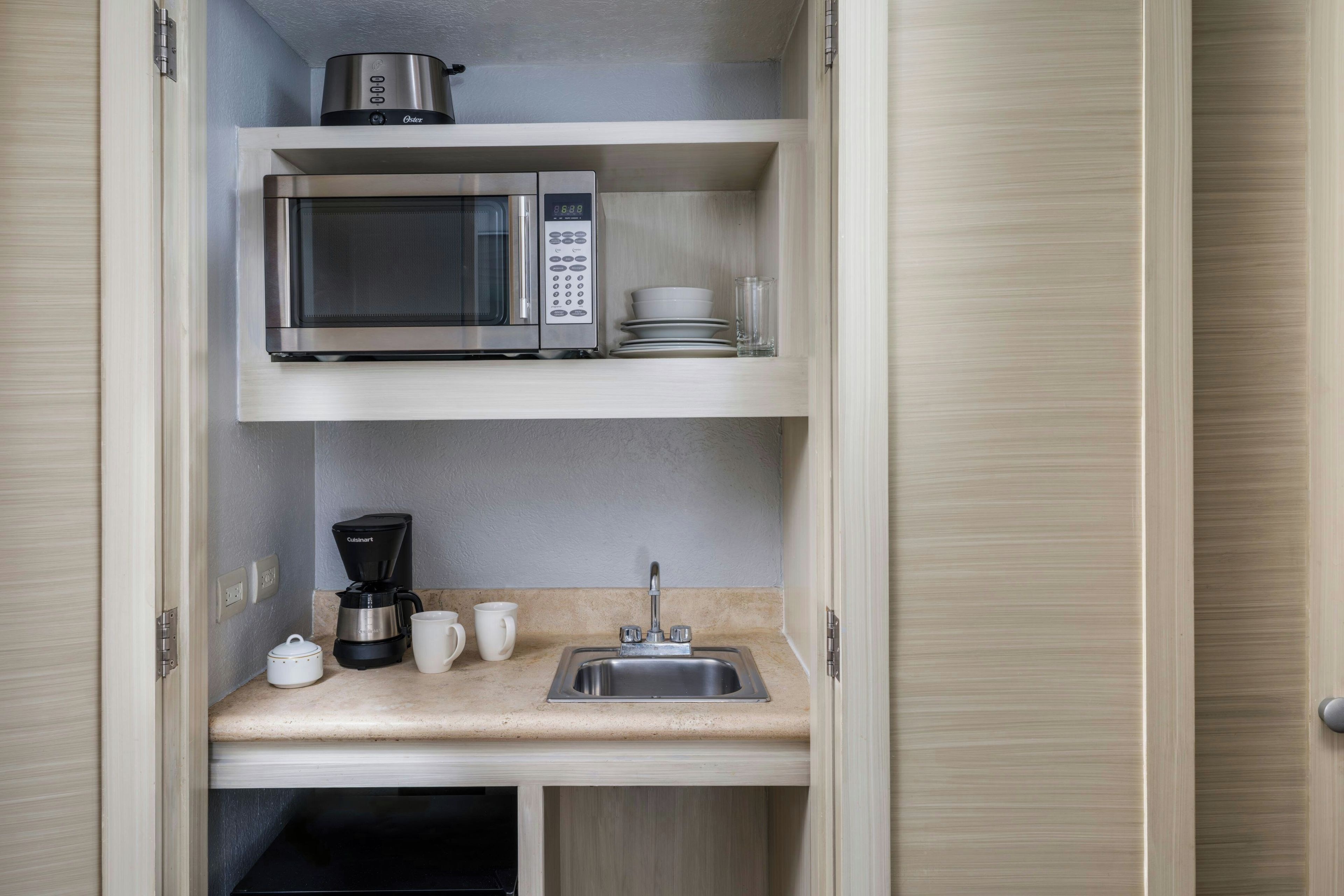 A compact kitchenette with a microwave, coffee maker, and a sink.