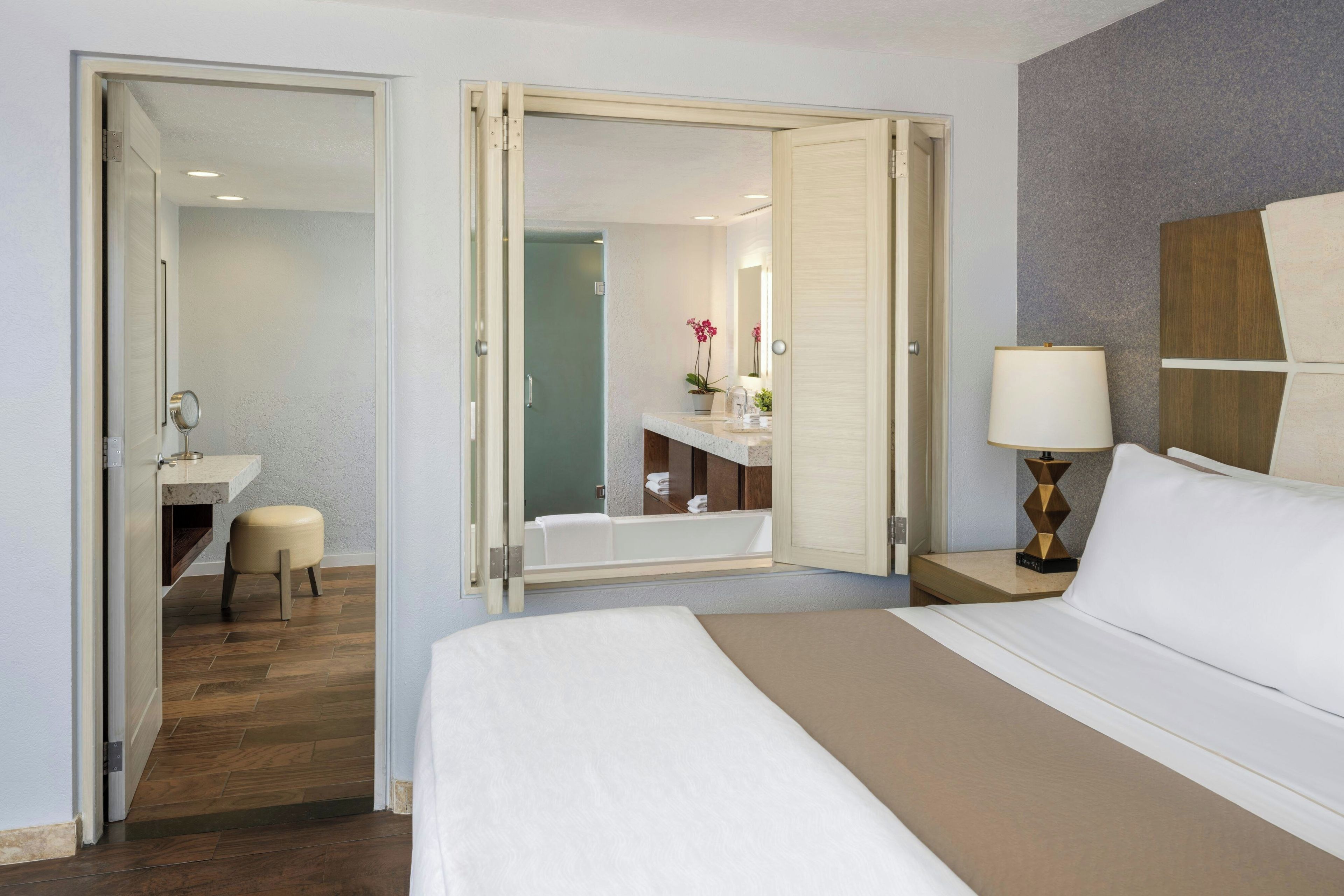 Habitación de hotel con cama, mesita de noche con lámpara, baño con bañera y espejo.
