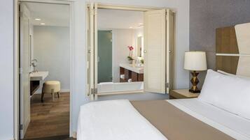 Een hotelkamer met een bed, nachtkastje met een lamp, een badkamer met bad en spiegel.