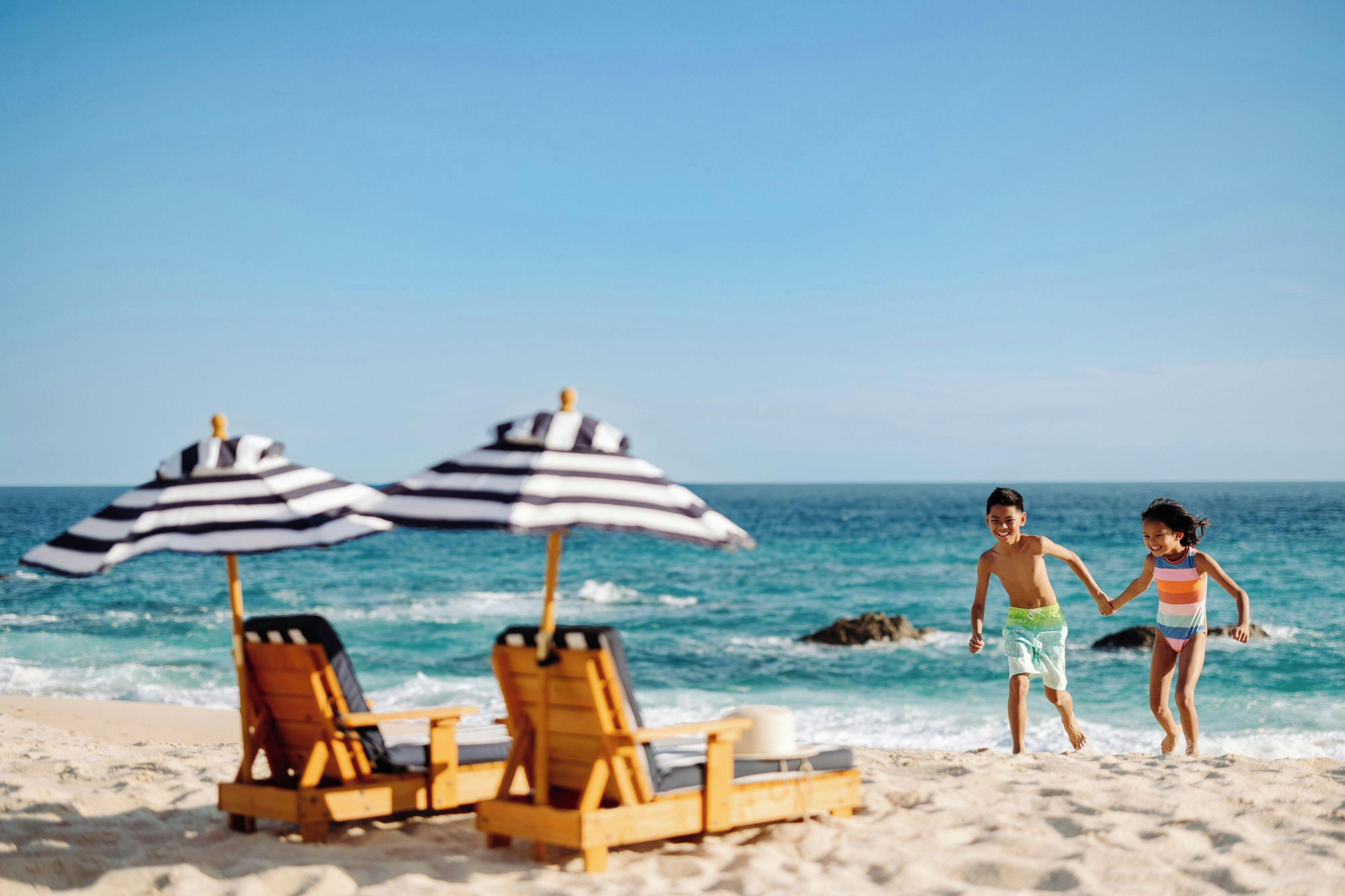 Une plage avec deux parasols rayés et des chaises longues en bois.
