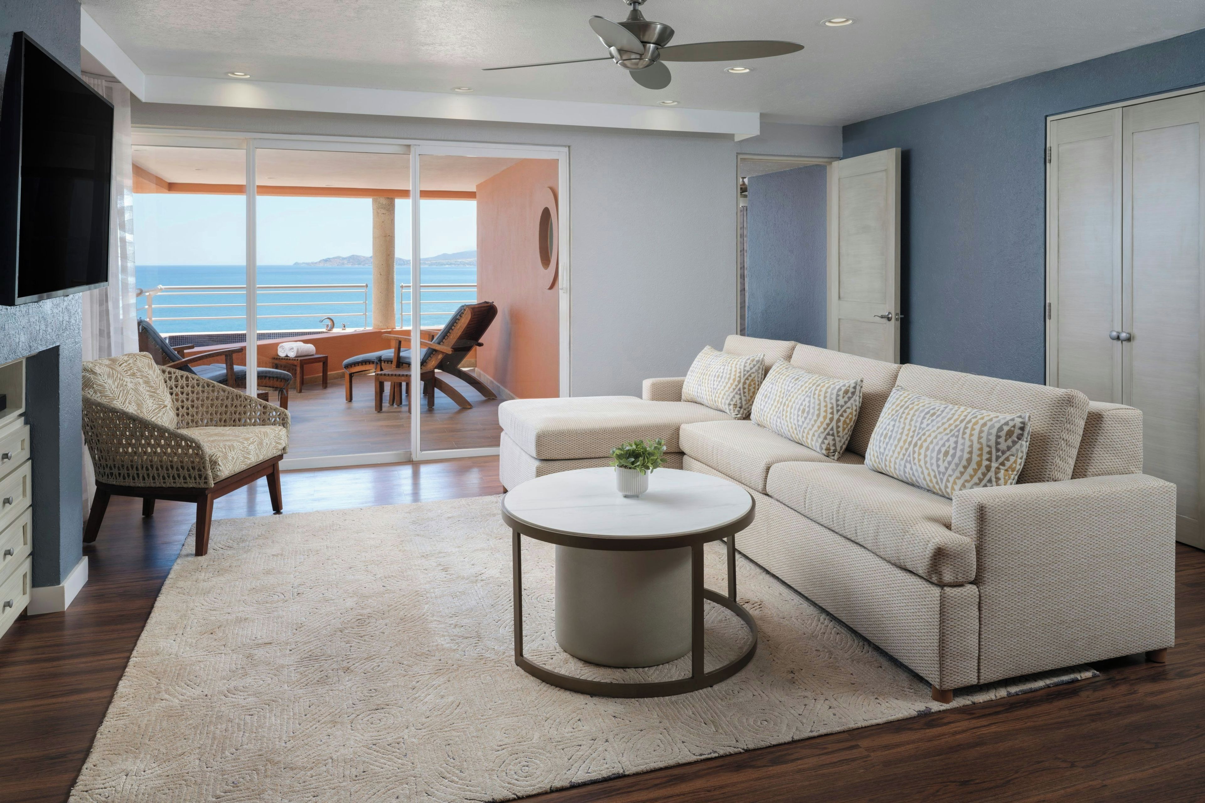 Una sala de estar moderna con un sofá, una mesa de centro y un televisor. Hay un balcón con vista al mar.