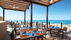 Un área de comedor al aire libre con mesas y sillas, con vista al océano.