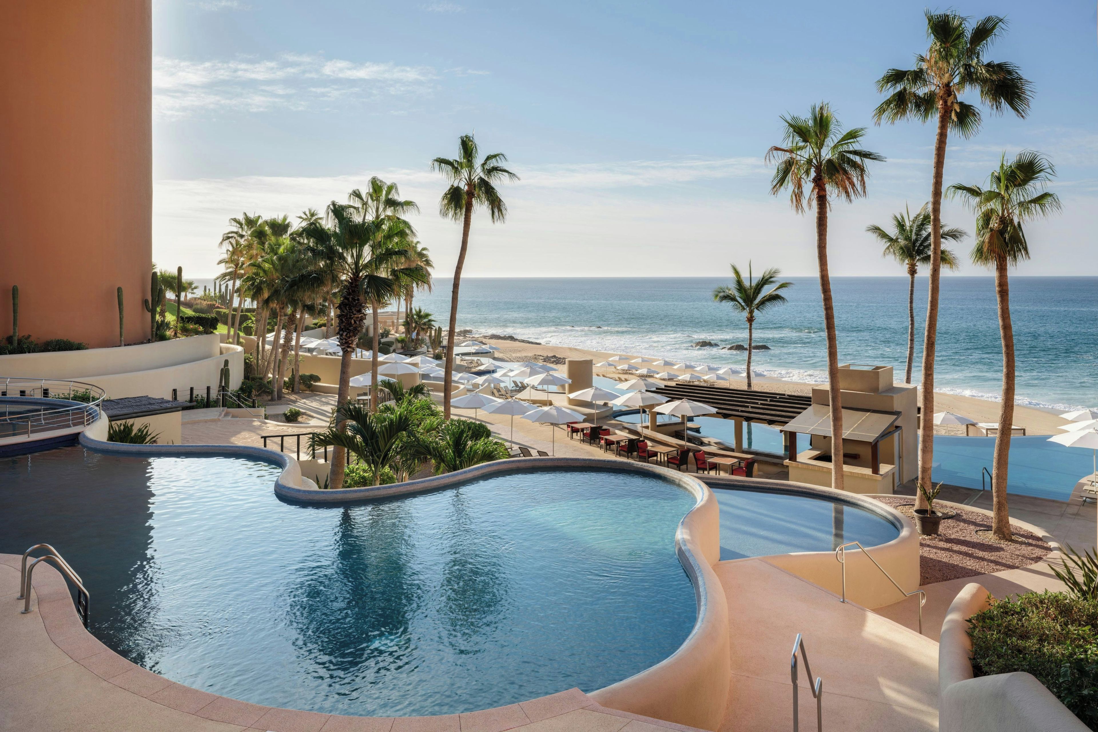A pool area with a view of the ocean, surrounded by palm trees and lounge chairs.