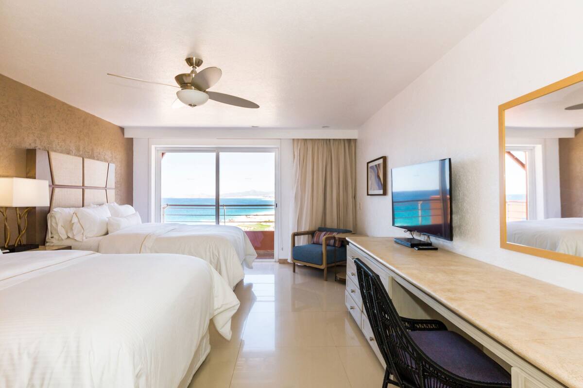 Ein Hotelzimmer mit zwei Betten, einem Fernseher, einem Schreibtisch und einem Sessel.