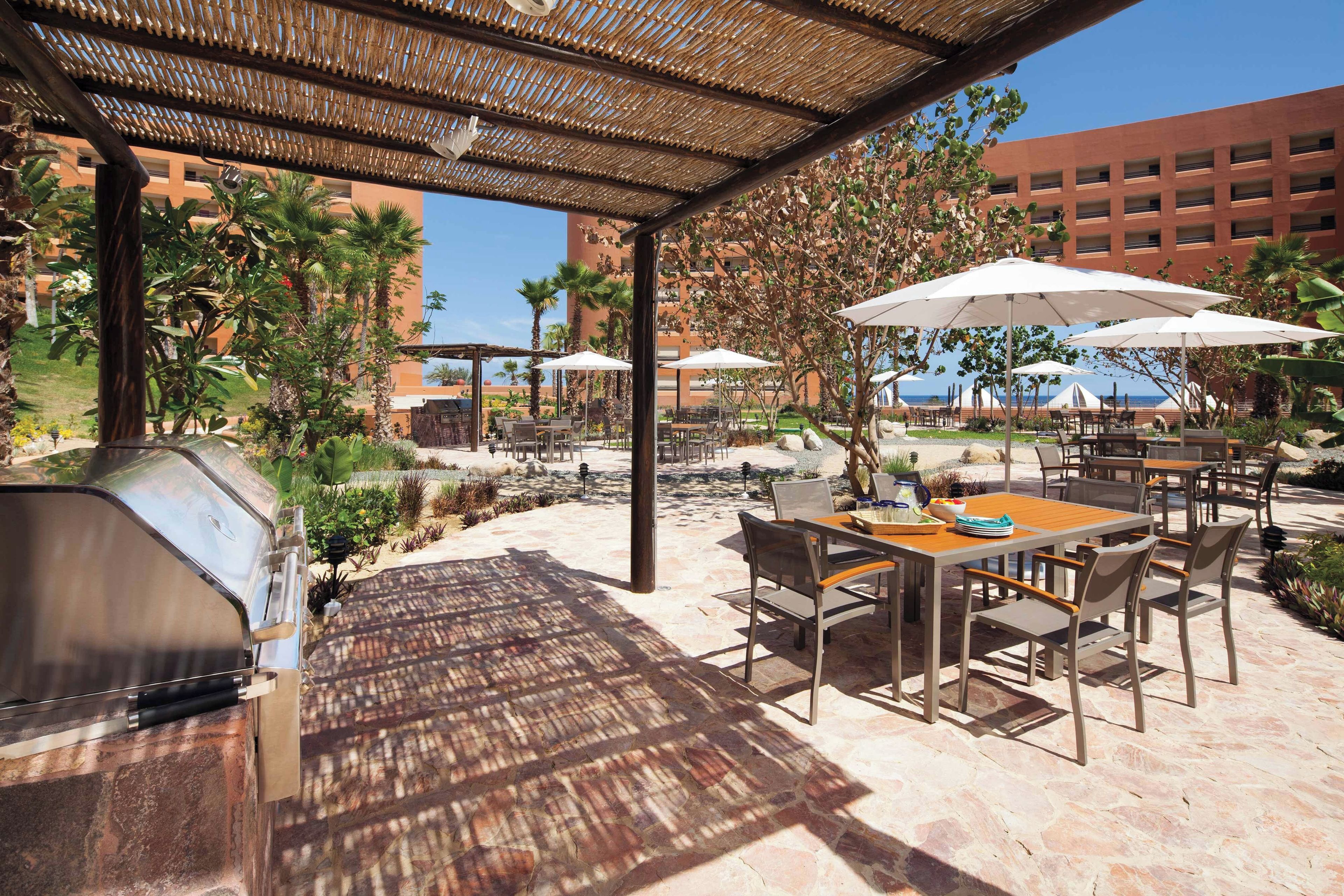 An outdoor patio with a barbecue grill, tables, and umbrellas.