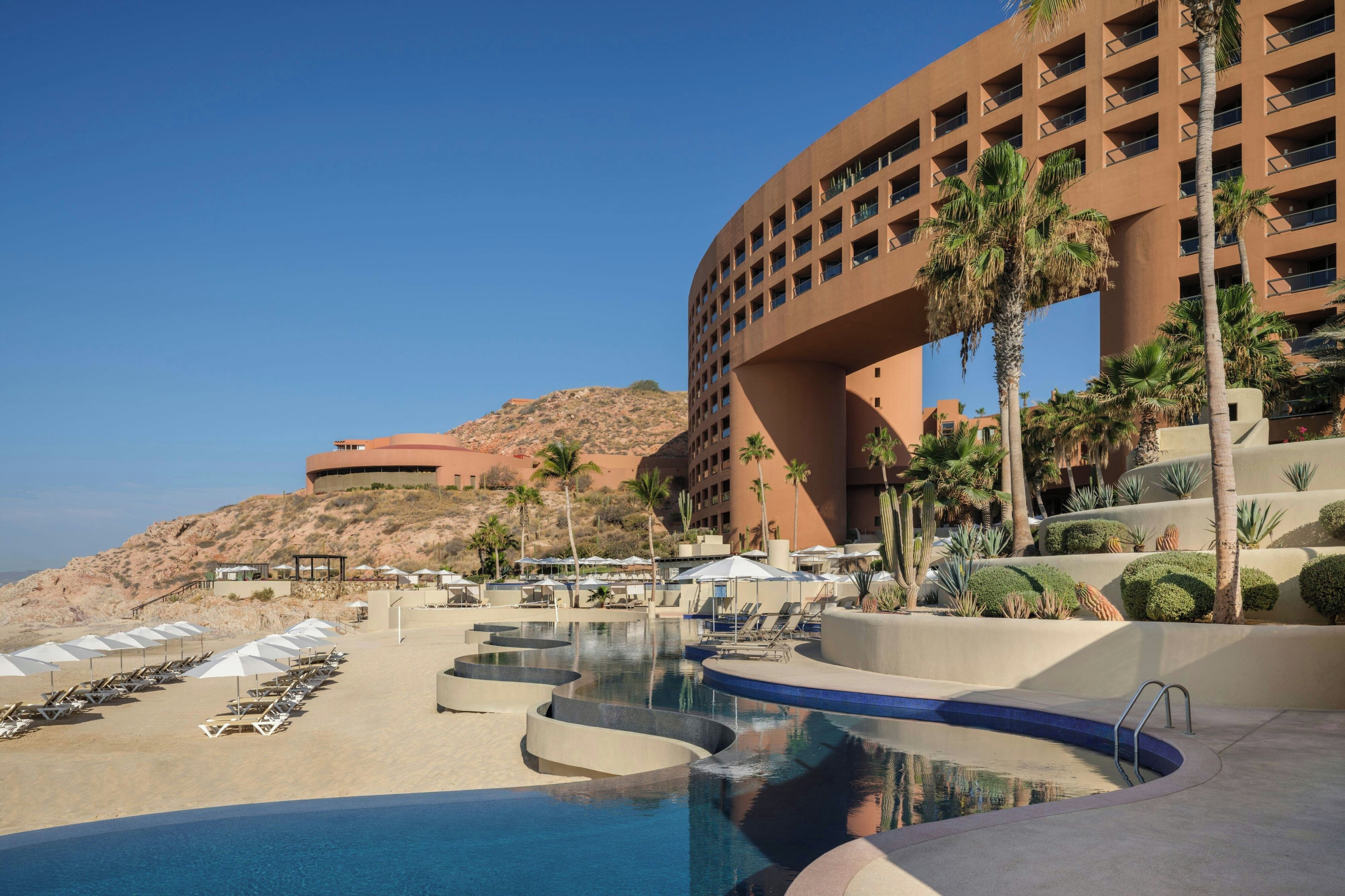 A resort with a pool, lounge chairs, and palm trees.