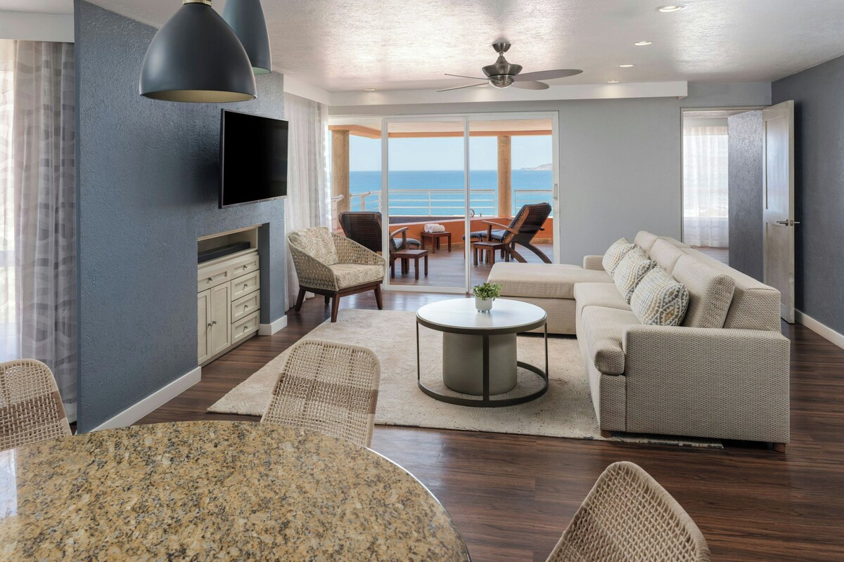 A modern living room with a flat-screen TV, a ceiling fan, and a view of the ocean.