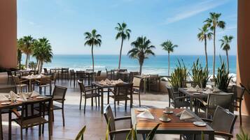 Un restaurante con terraza al aire libre que da al océano, con palmeras y vistas despejadas al mar.