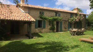 A rustic stone building with a tiled roof, a covered patio, and a grassy yard with outdoor furniture. - Charming country house (Verruyes)