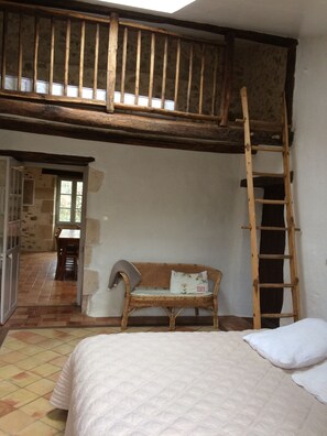 A bedroom with a loft area, a wooden ladder, a wicker sofa, and a bed with a quilted cover. - Charming country house (Verruyes)