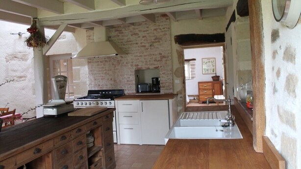 A kitchen with a brick wall, wooden cabinets, a stove, and a sink. - Charming country house (Verruyes)