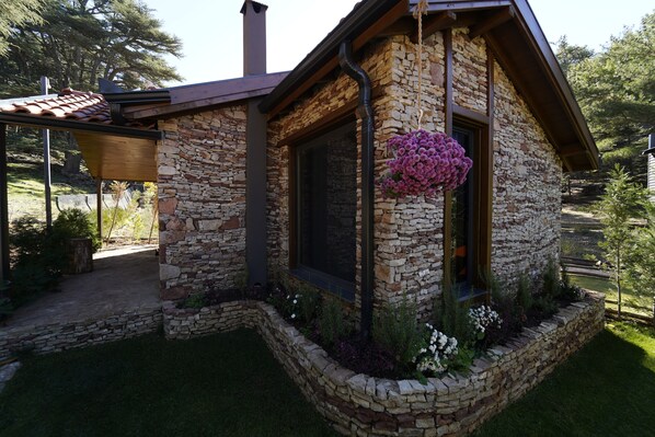 A stone house with a sloped roof, a window with a hanging flower, and a stone foundation. - Cragus Inn (Fethiye)