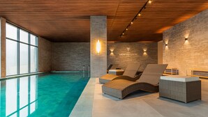 A modern indoor swimming pool area with lounge chairs and a visible logo on the wall. - Laghetto Canela (Canela)
