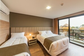 Habitación de hotel con dos camas, una mesita de noche con lámpara y un ventanal con vistas a la ciudad.