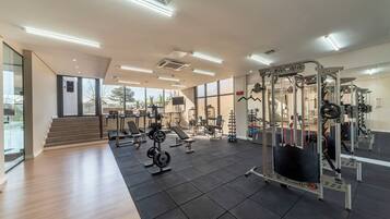 Ein modernes Fitnessstudio mit verschiedenen Trainingsgeräten, großen Fenstern und einer Treppe, die zu einer oberen Ebene führt.