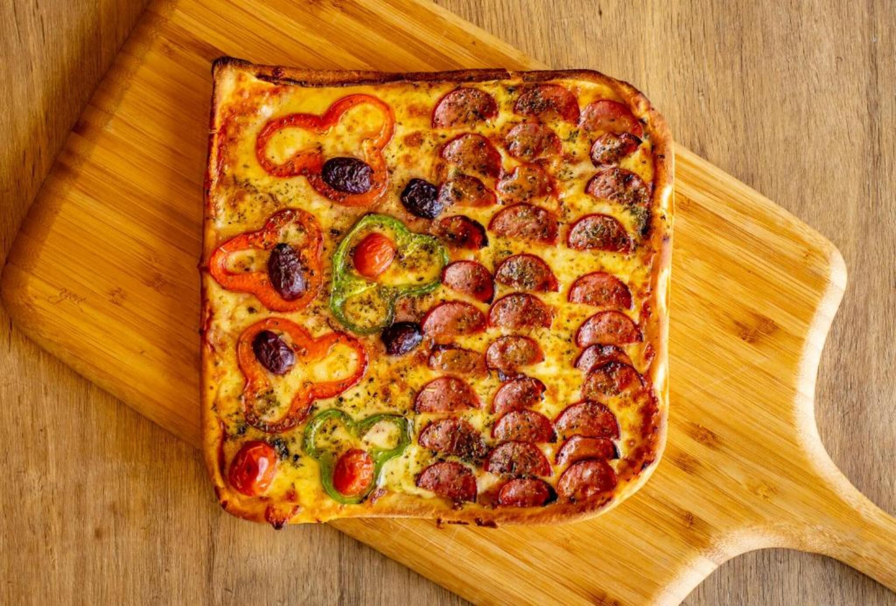 A square pizza with pepperoni and bell peppers on a wooden board.