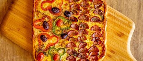 A square pizza with pepperoni and bell peppers on a wooden board.