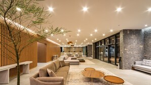 A modern lobby with a sectional sofa, round coffee tables, and a large tree. - Laghetto Canela (Canela)