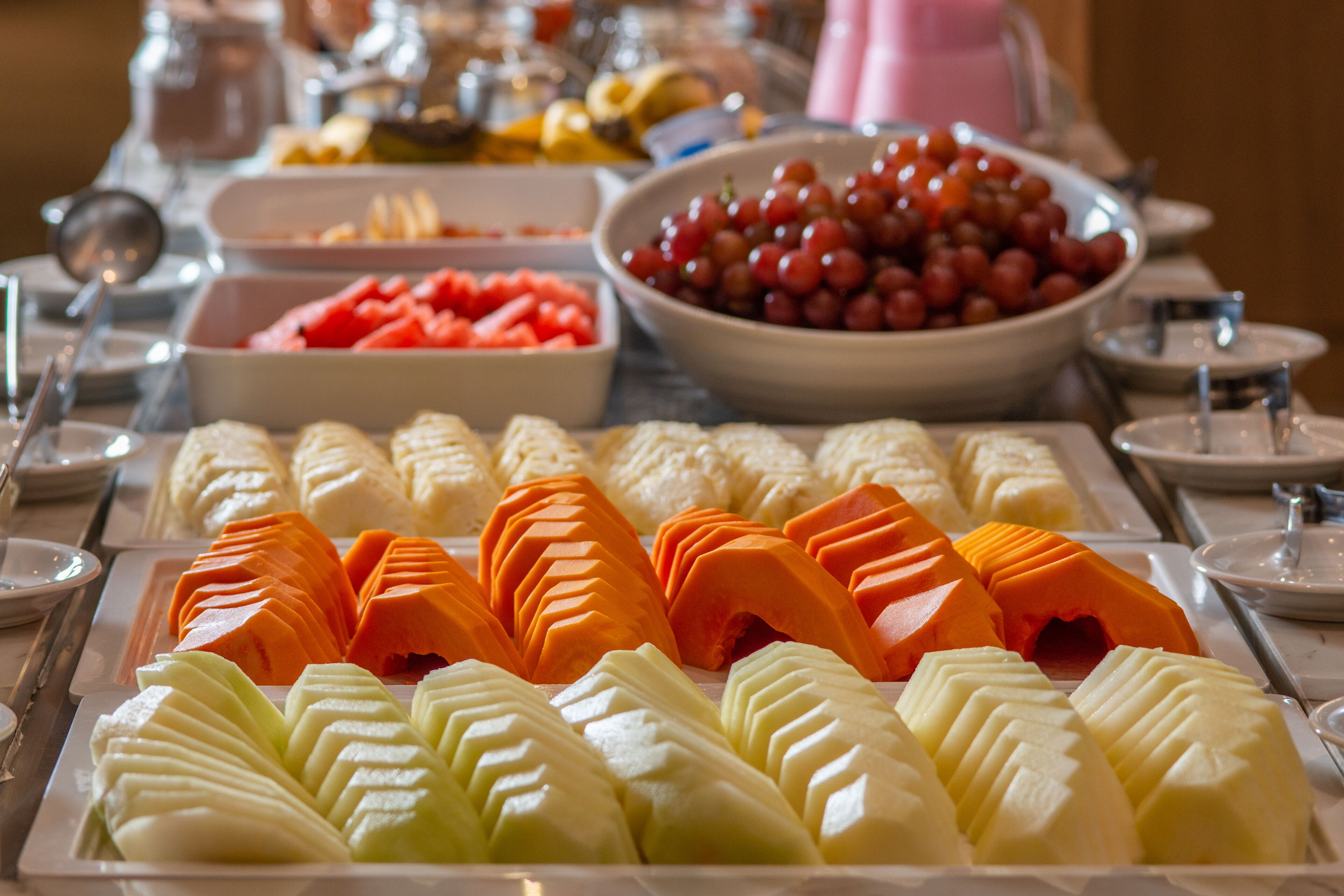 A buffet with various fruits and vegetables, including sliced carrots, apples, and grapes.