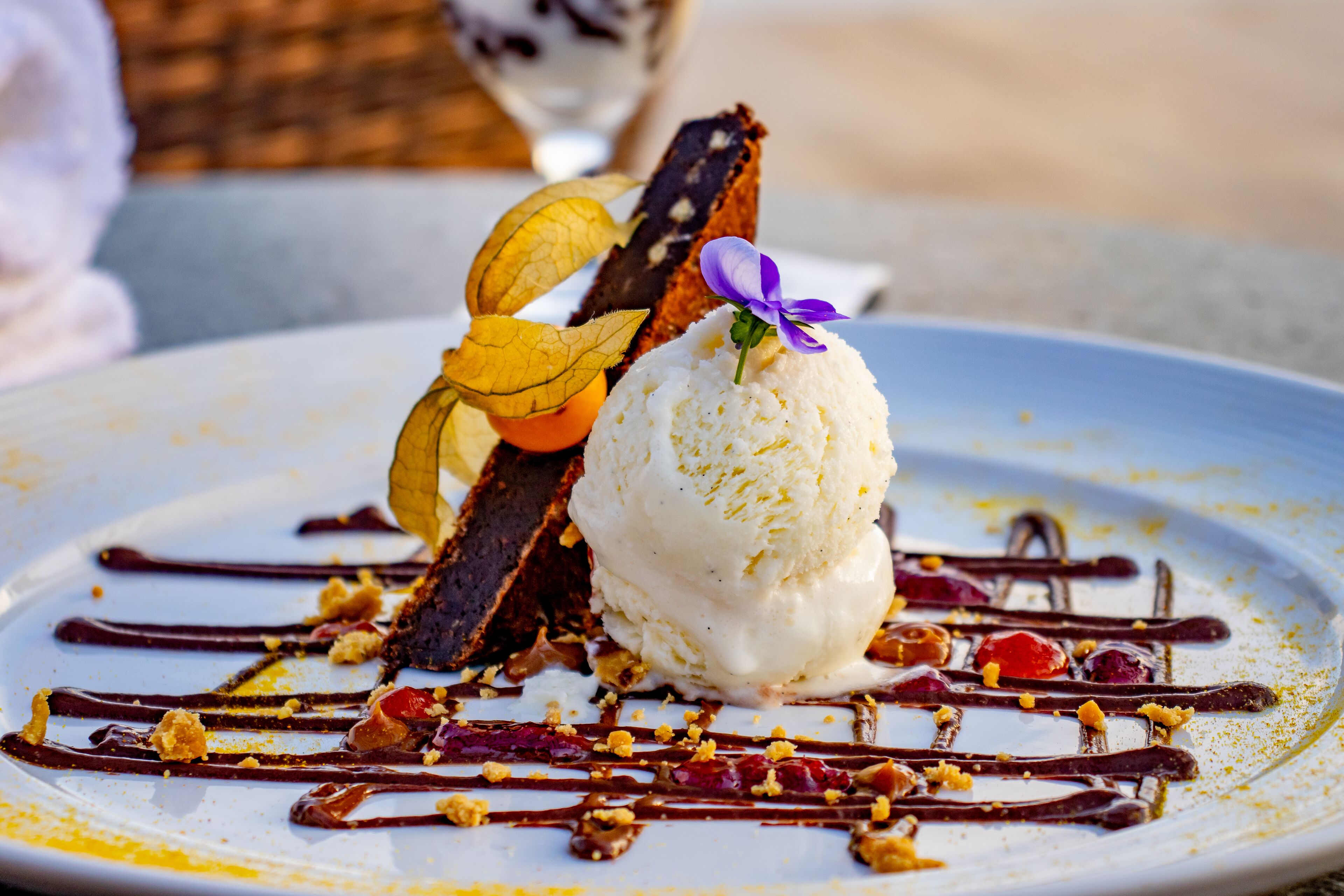 Un plato de postre con helado, salsa de chocolate y guarniciones de frutas.