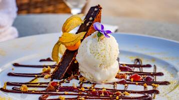 Un plato de postre con helado, salsa de chocolate y guarniciones de frutas.