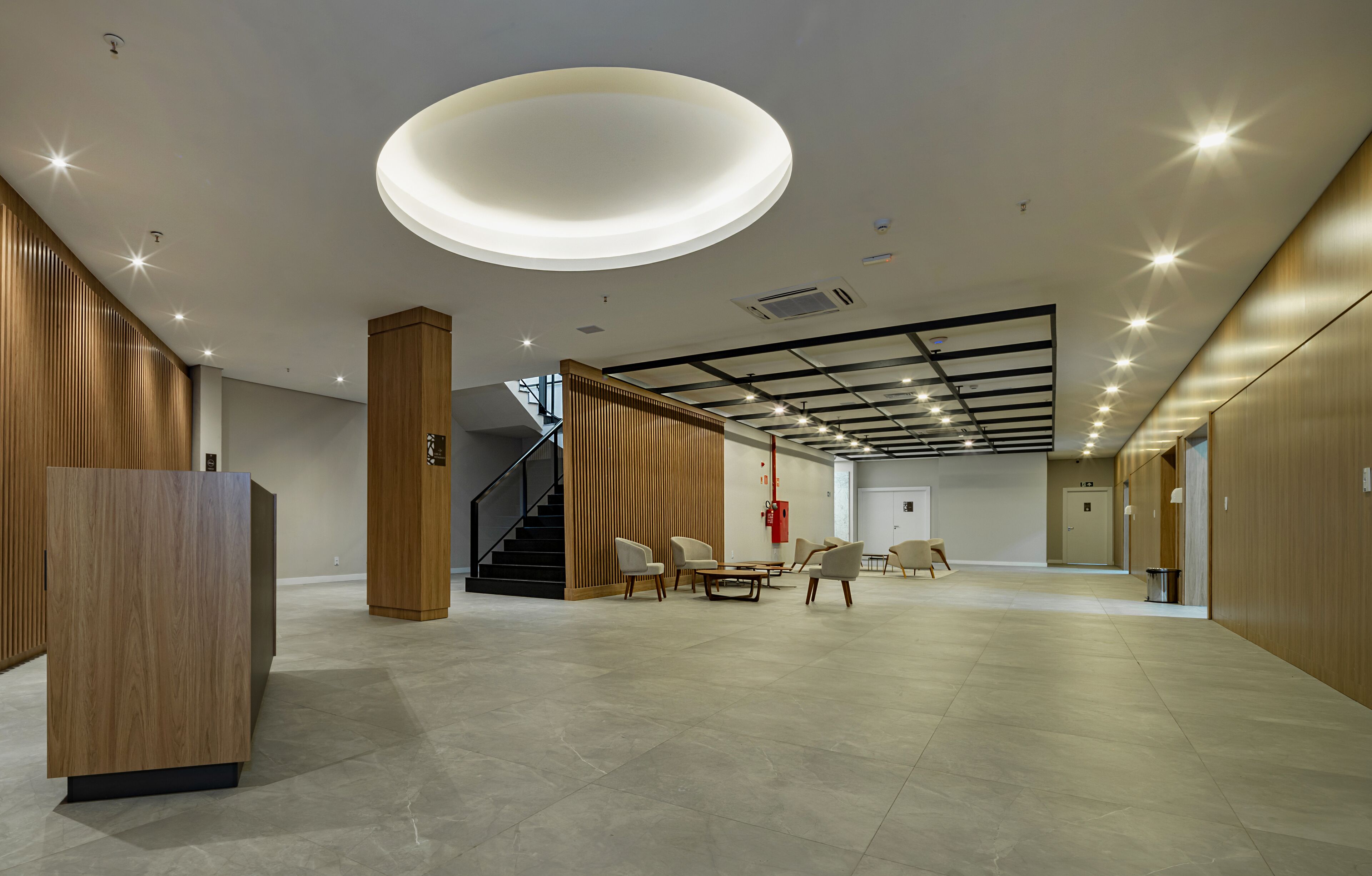 A spacious lobby with a modern design, featuring a large reception desk, seating area, and a staircase.