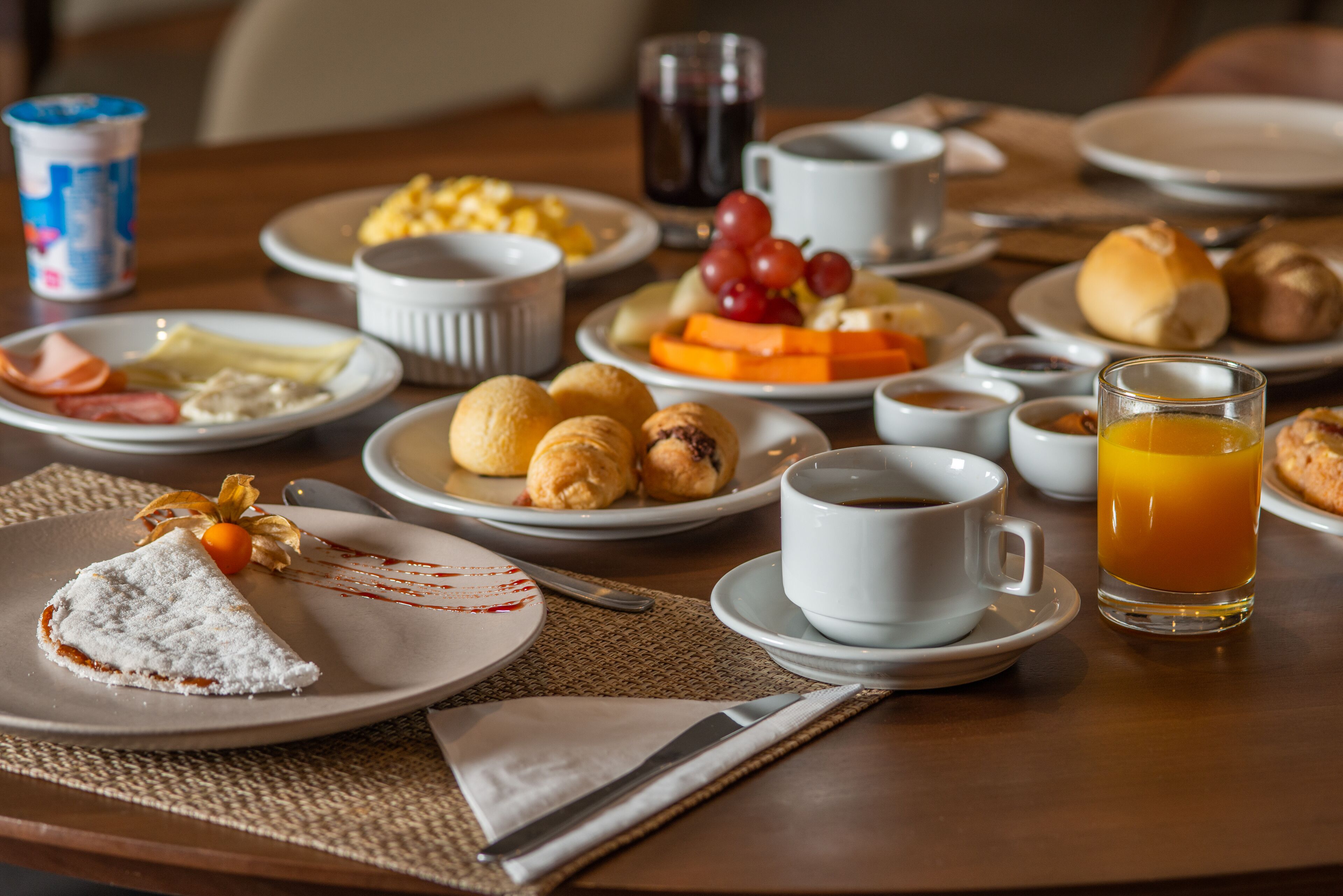 Una mesa de desayuno con platos de comida, una taza de café y un vaso de jugo de naranja.