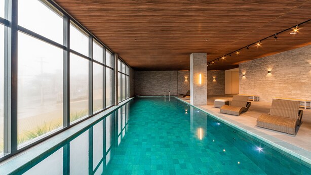 A modern indoor swimming pool with clear glass walls, wooden ceiling, and lounge chairs. - Laghetto Canela (Canela)
