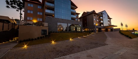 Un hotel moderno con una estructura de varios pisos, un camino pavimentado y un área ajardinada con árboles.