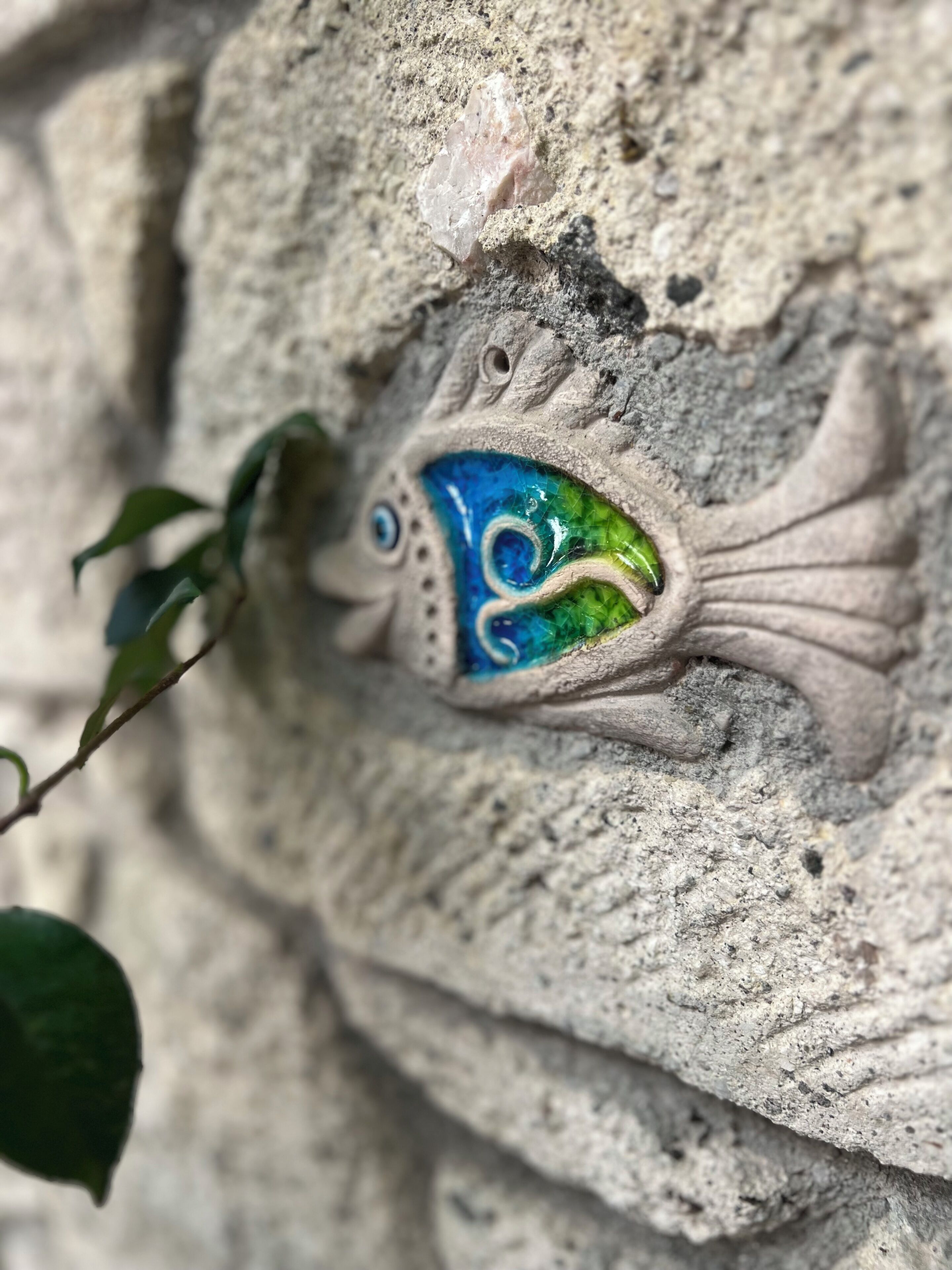 A stone sculpture of a fish with a blue and green design.