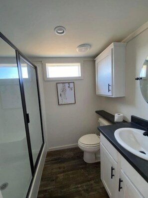 A bathroom with a glass shower enclosure, a toilet, a sink with a black countertop, and a window above the toilet. - Hales Bar Marina and Resort (Guild)