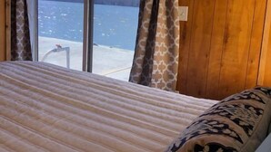 A bed with a patterned pillow, a view of a body of water, and wooden walls. - Hales Bar Marina and Resort (Guild)