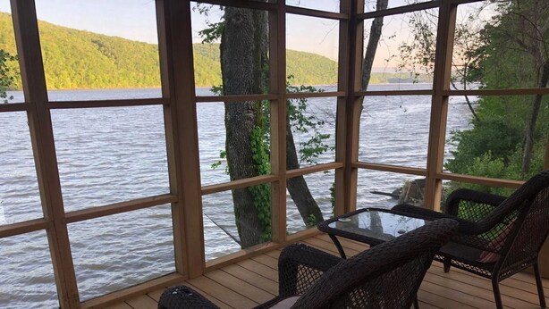 A covered outdoor seating area with wicker chairs and a glass table, overlooking a lake with trees and hills in the background. - Hales Bar Marina and Resort (Guild)