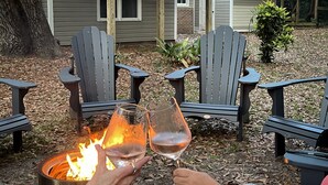 A fire pit with two glasses of wine, surrounded by Adirondack chairs.